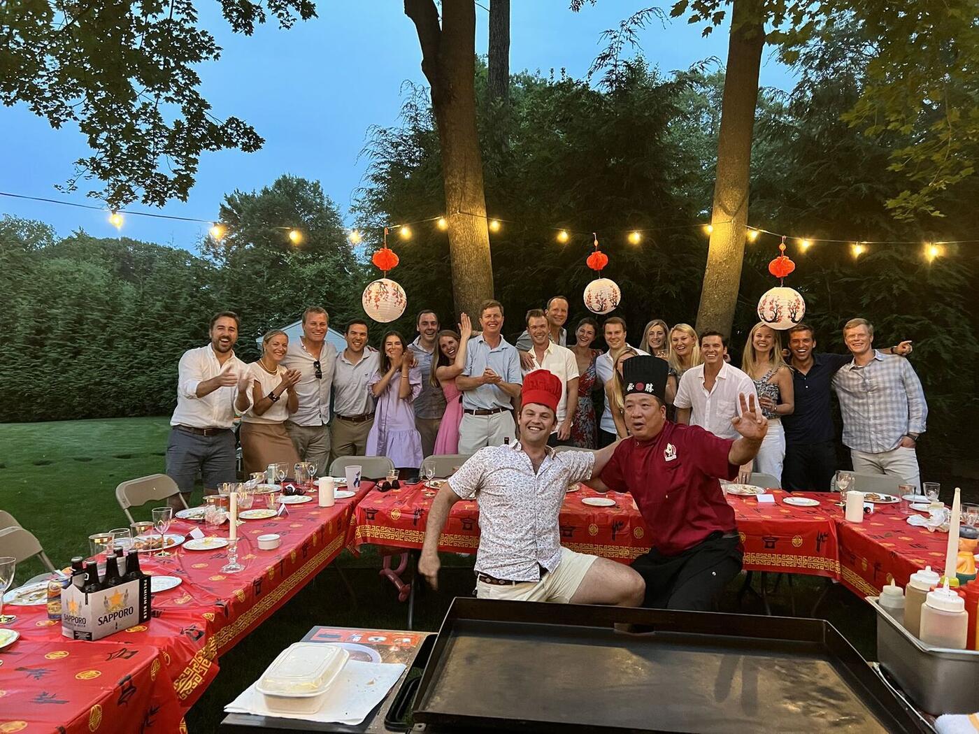 Guests and Happy Hibachi chef at a backyard hibachi party under string lights on Long Island